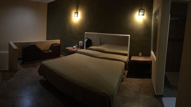 A hotel room with a large bed, a chair, a small table, and two wall-mounted lights. - El Fuerte Motel (Acapulco)