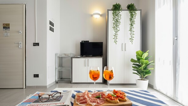 A modern room with a television, a cabinet with plants, a dining area with a newspaper, glasses, and food. - Da Bruno (Imperia)