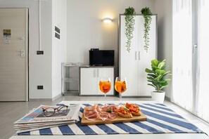Una habitación moderna con televisor, un mueble con plantas, un área de comedor con periódico, vasos y comida.