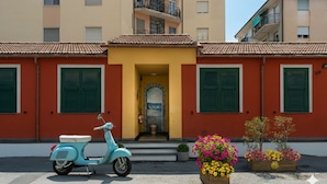 A vintage scooter parked in front of a building with a yellow entrance and green shutters. - Da Bruno (Imperia)
