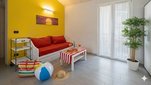 A bright yellow room with a white sofa, a striped table, a beach ball, a beach hat, and a potted plant. - Da Bruno (Imperia)