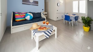 A modern living room with a sofa, a dining table with chairs, a small table with a pizza and drinks, and a potted plant. - Da Bruno (Imperia)