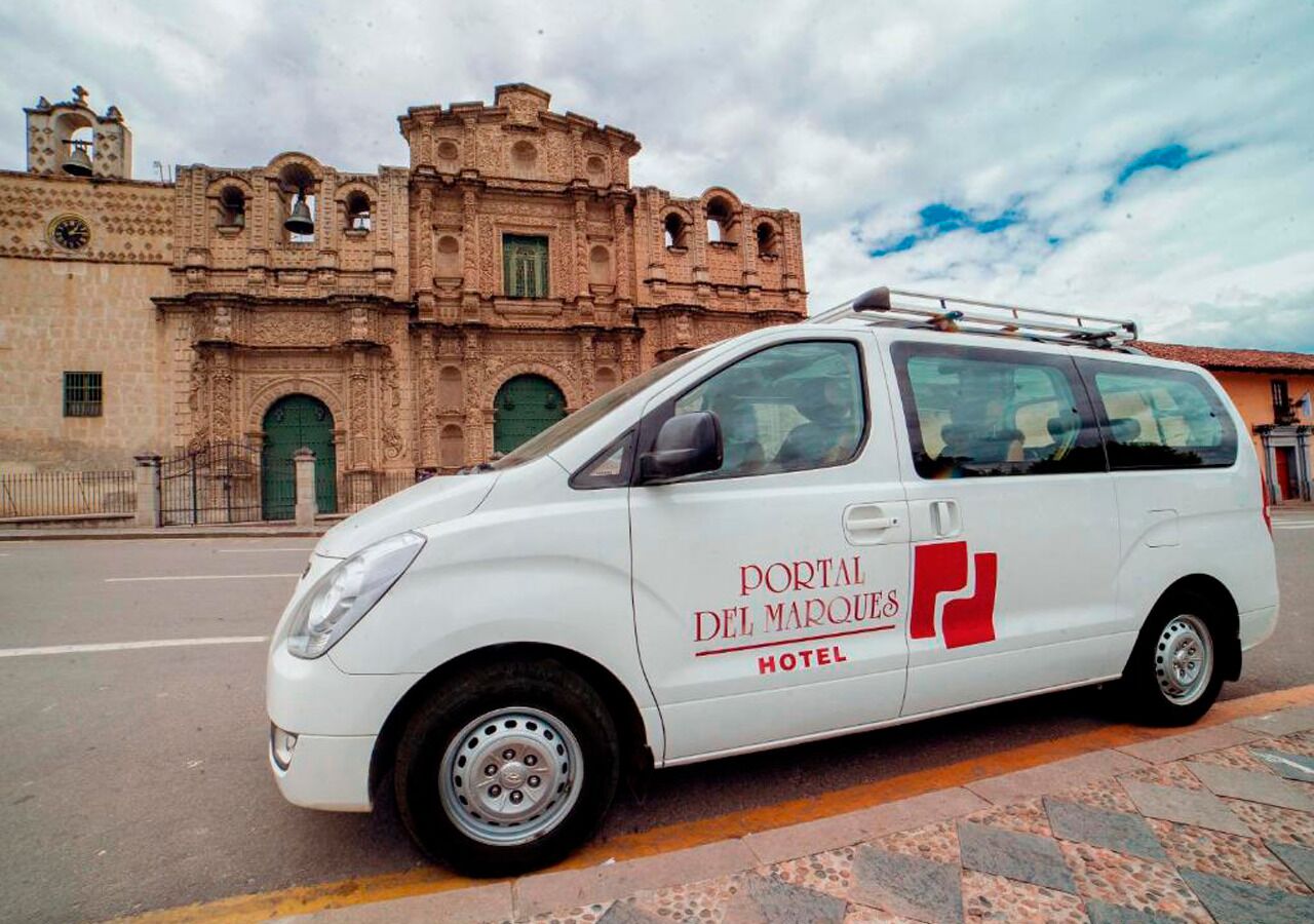 A white van with "Portal Del Marques Hotel" branding parked in front of a historic building with arched windows and bell towers.