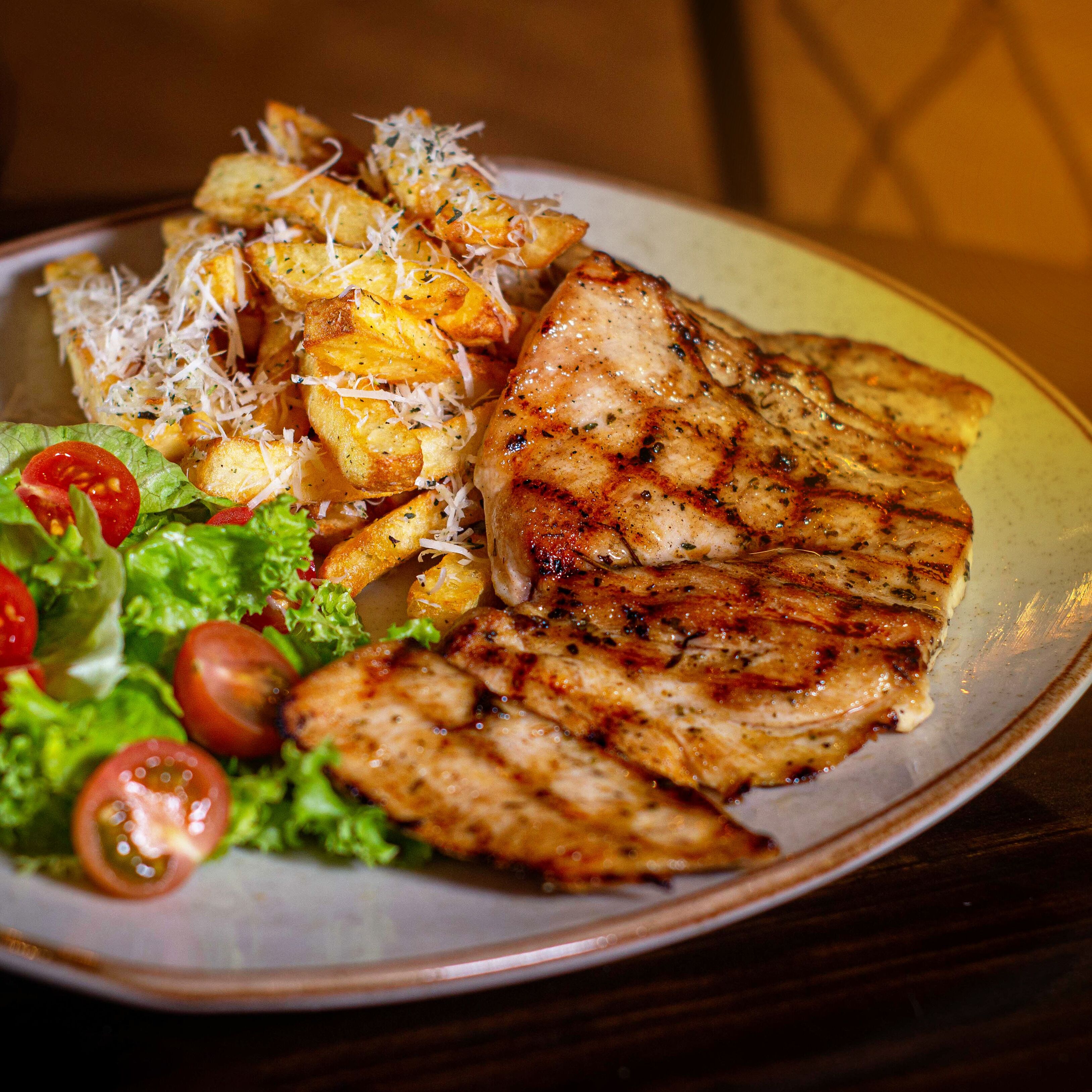 A plate of grilled chicken, roasted potatoes, and a side salad with lettuce and cherry tomatoes.