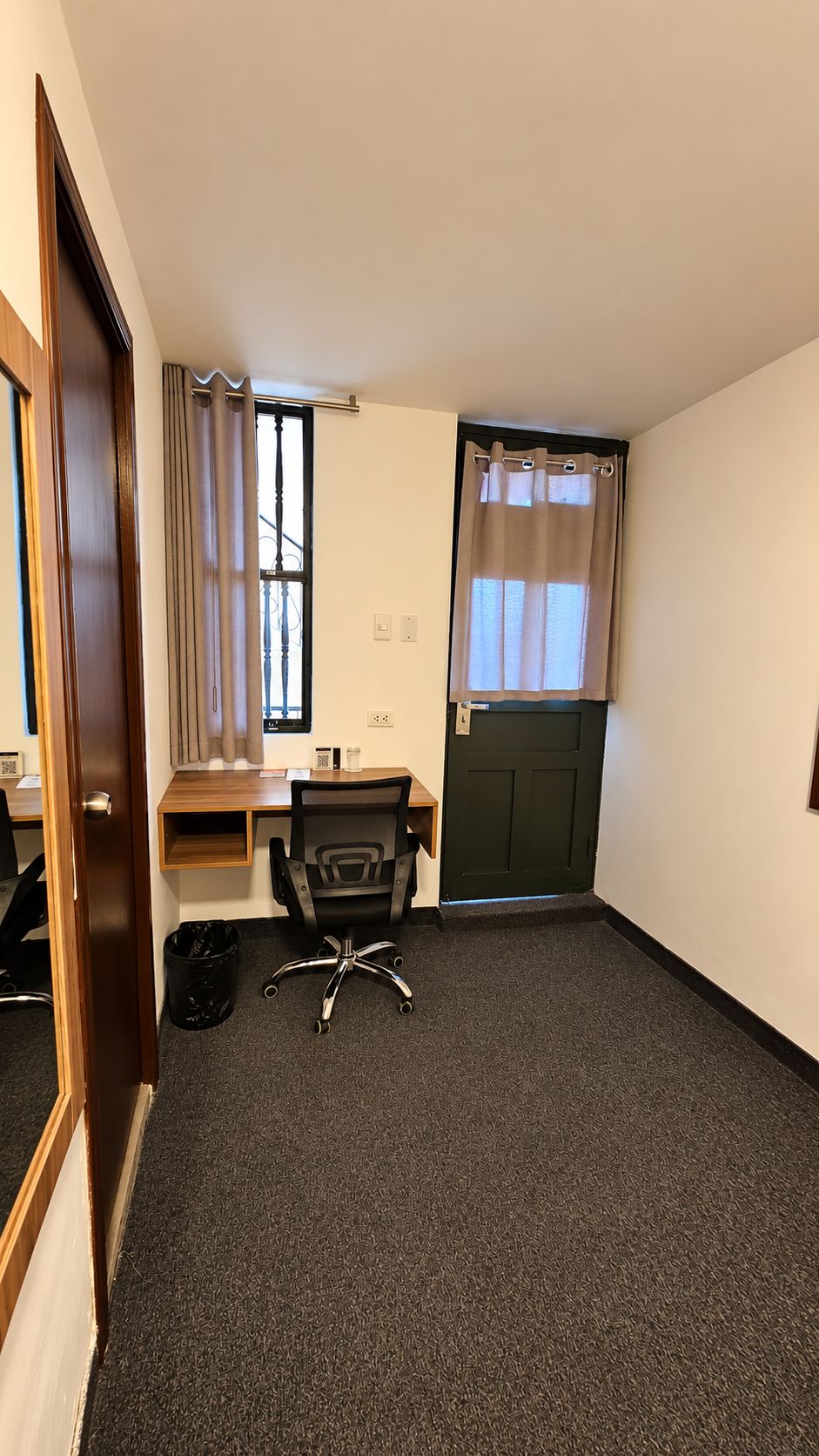 A small, compact room with a desk, chair, and a window with curtains.