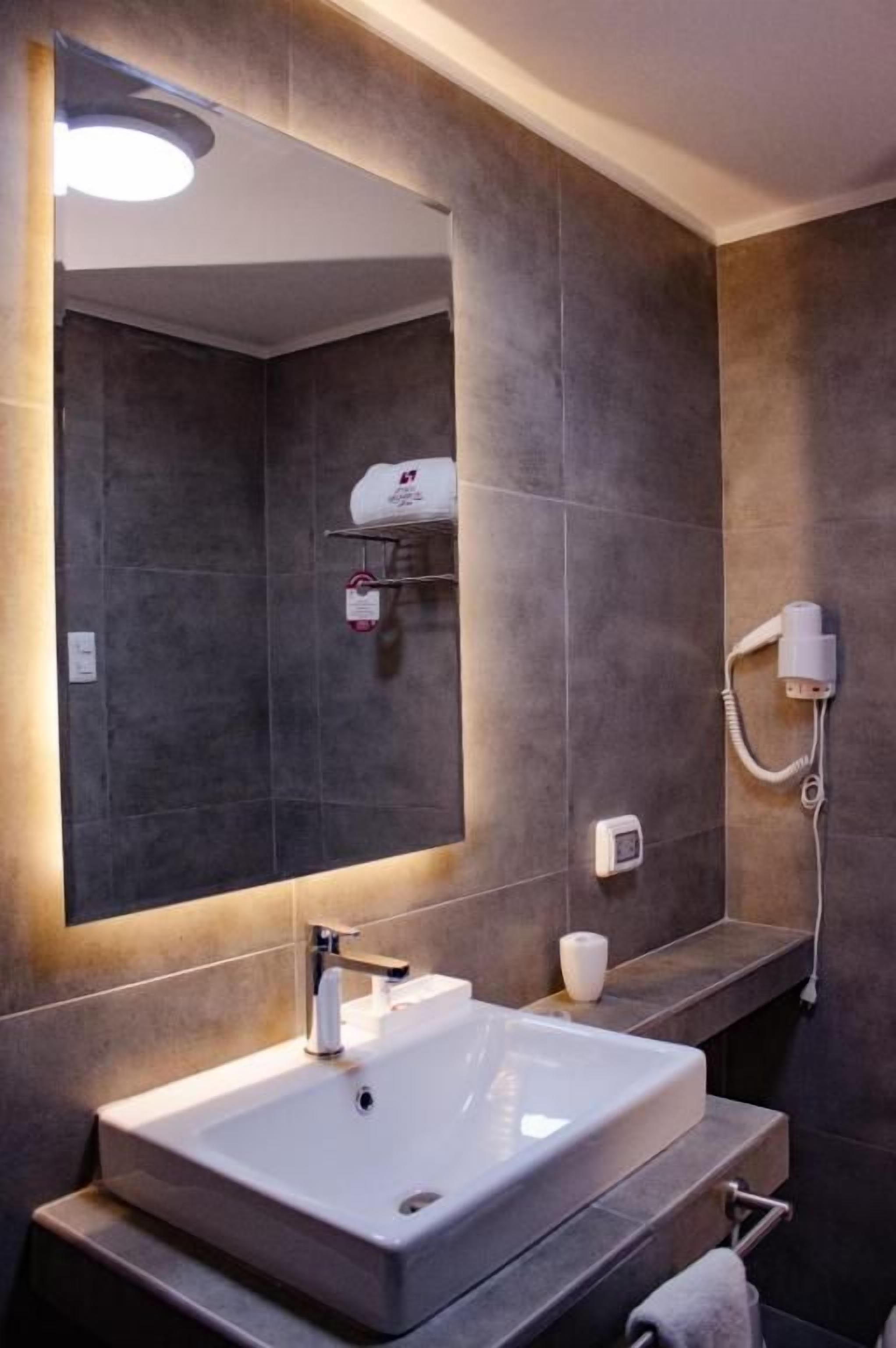 A modern bathroom with a large mirror, a white sink, and a towel rack.