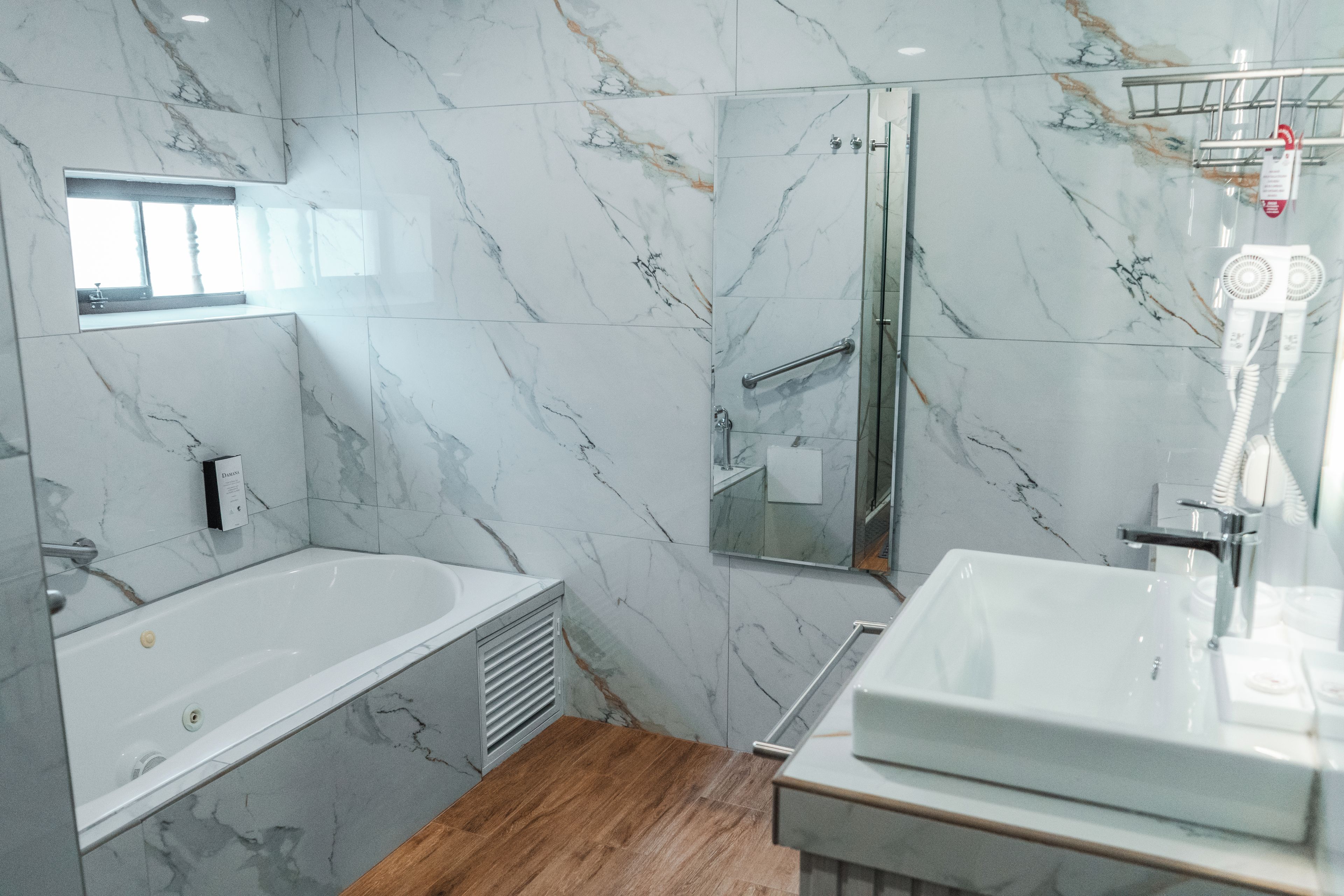A modern bathroom with a marble wall, a bathtub, a shower, and a sink.