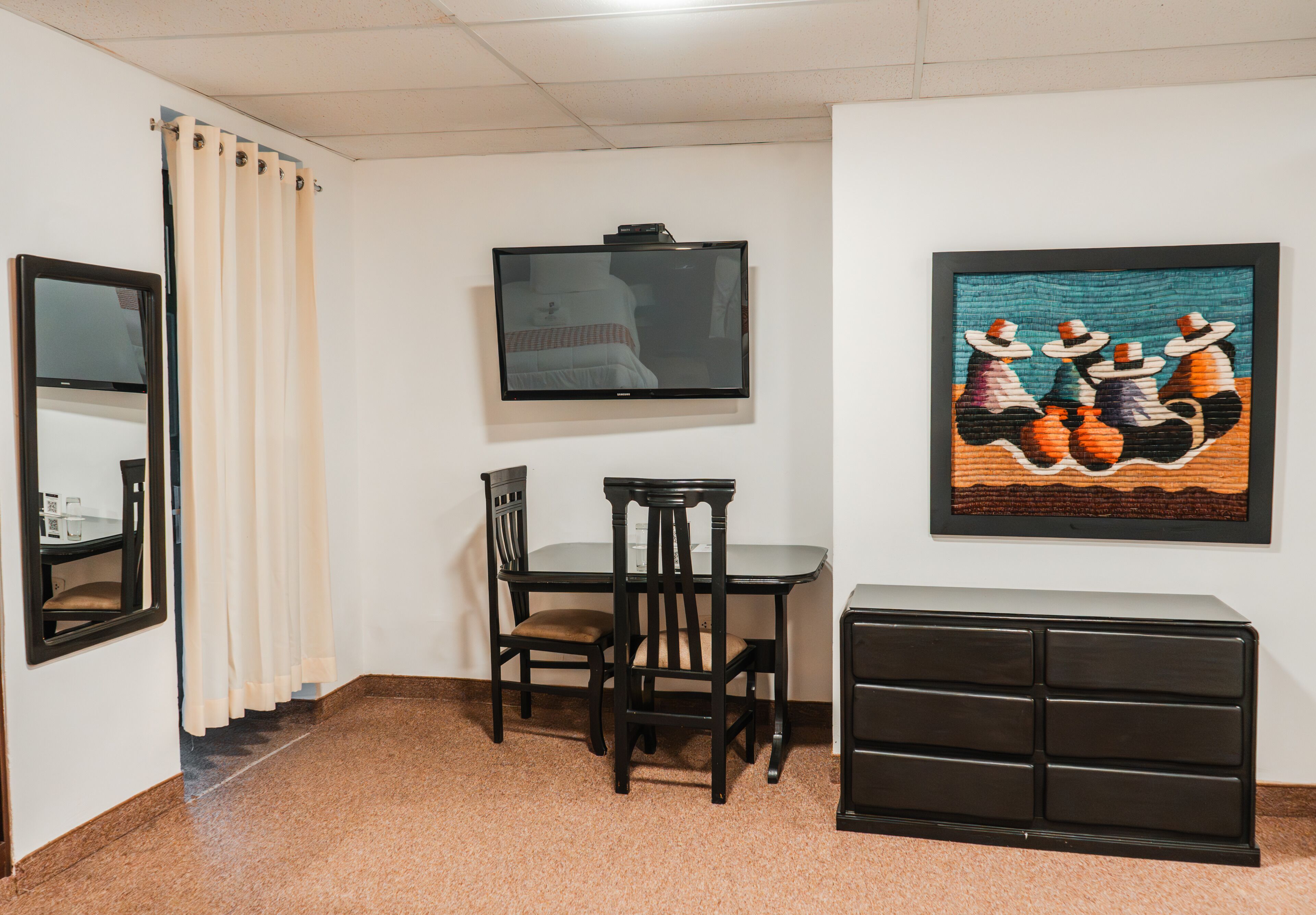 A room with a bed, a desk with a chair, a television, a framed artwork, and a dresser.