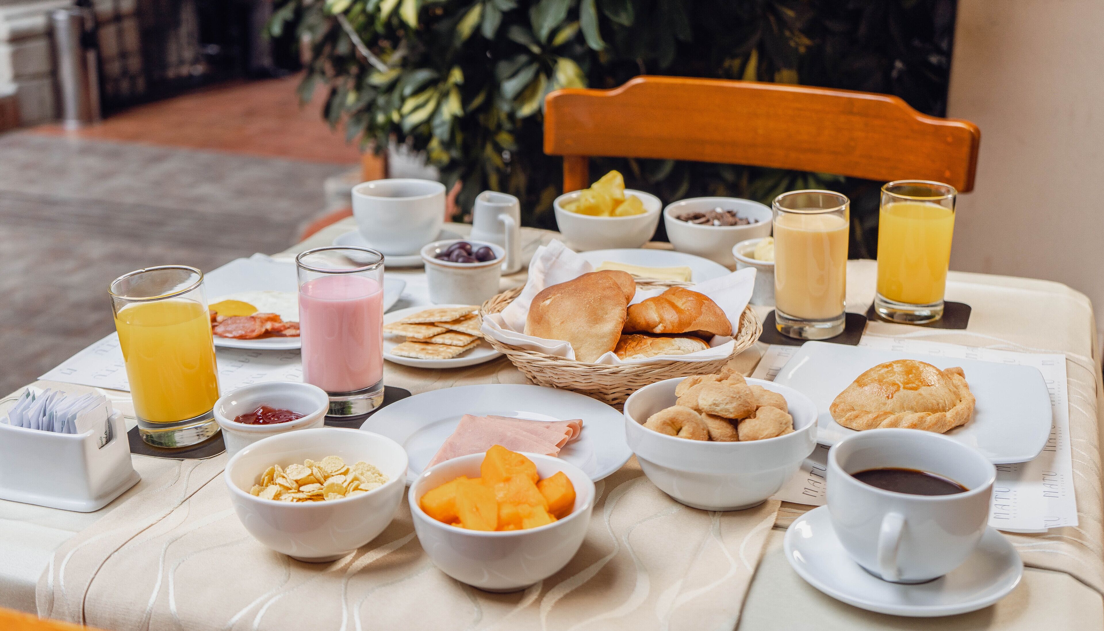 Una tavola imbandita con diversi cibi e bevande, tra cui cereali, frutta, pasticcini e caffè.