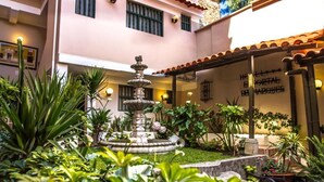 Un patio con una fuente central, rodeado de abundante vegetación y un edificio de techo a tejas.