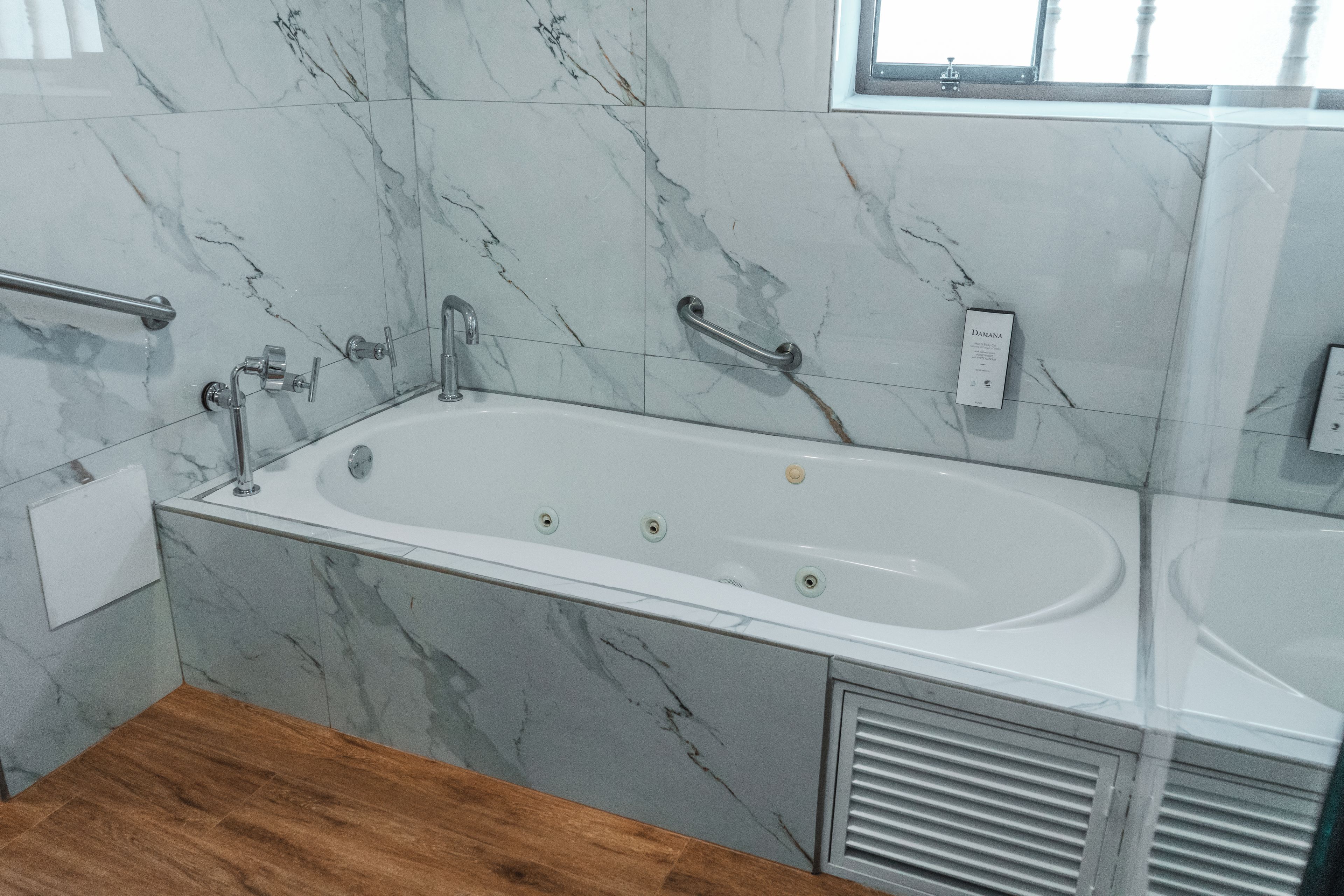 Une salle de bain avec un mur en marbre, une baignoire, une douche et un plancher en bois.