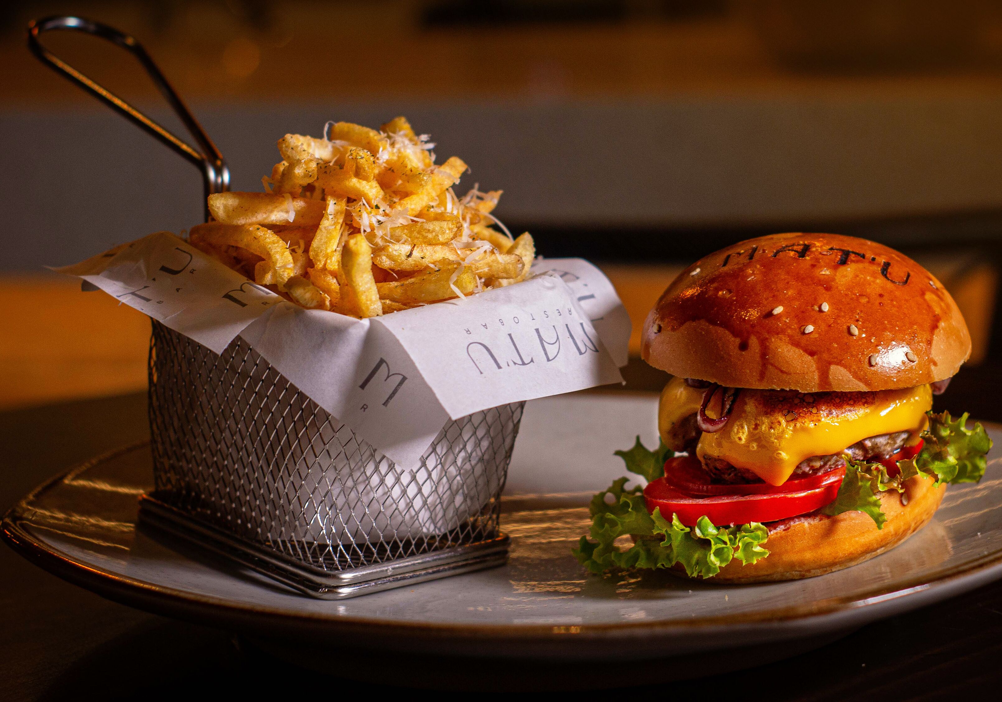 A burger with cheese and lettuce on a bun, and a basket of fries with a paper label.