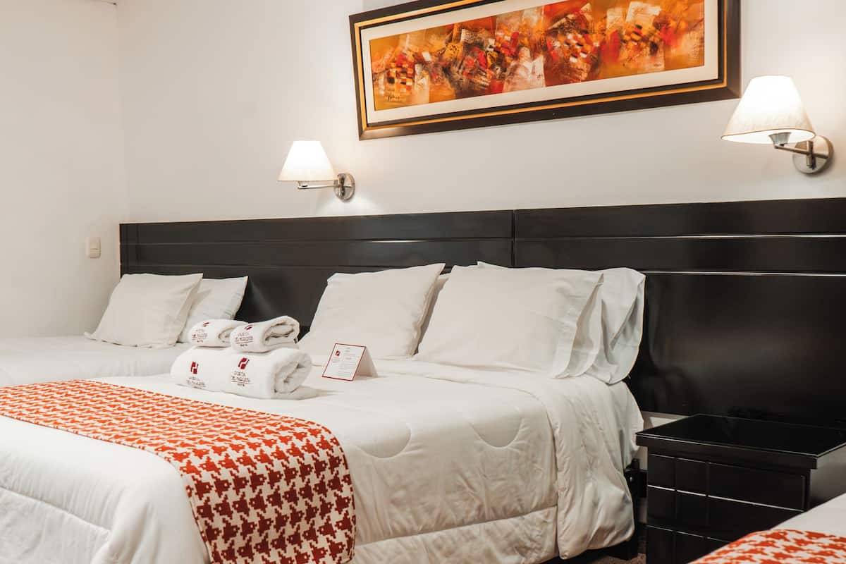 A hotel room with two beds, a large painting on the wall, and a nightstand with a lamp.