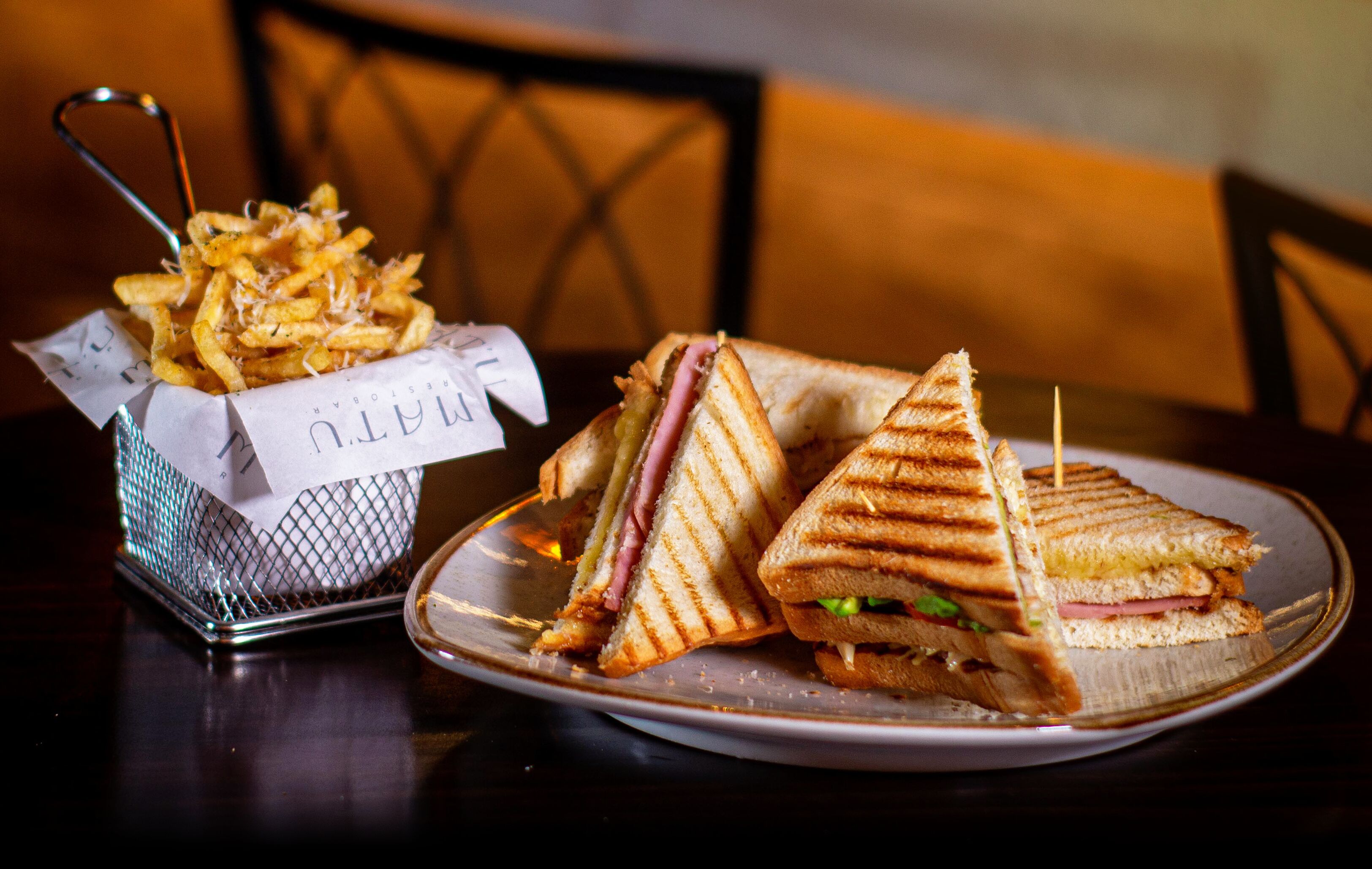 Un plato con un sándwich a la plancha y una cesta de papas fritas.