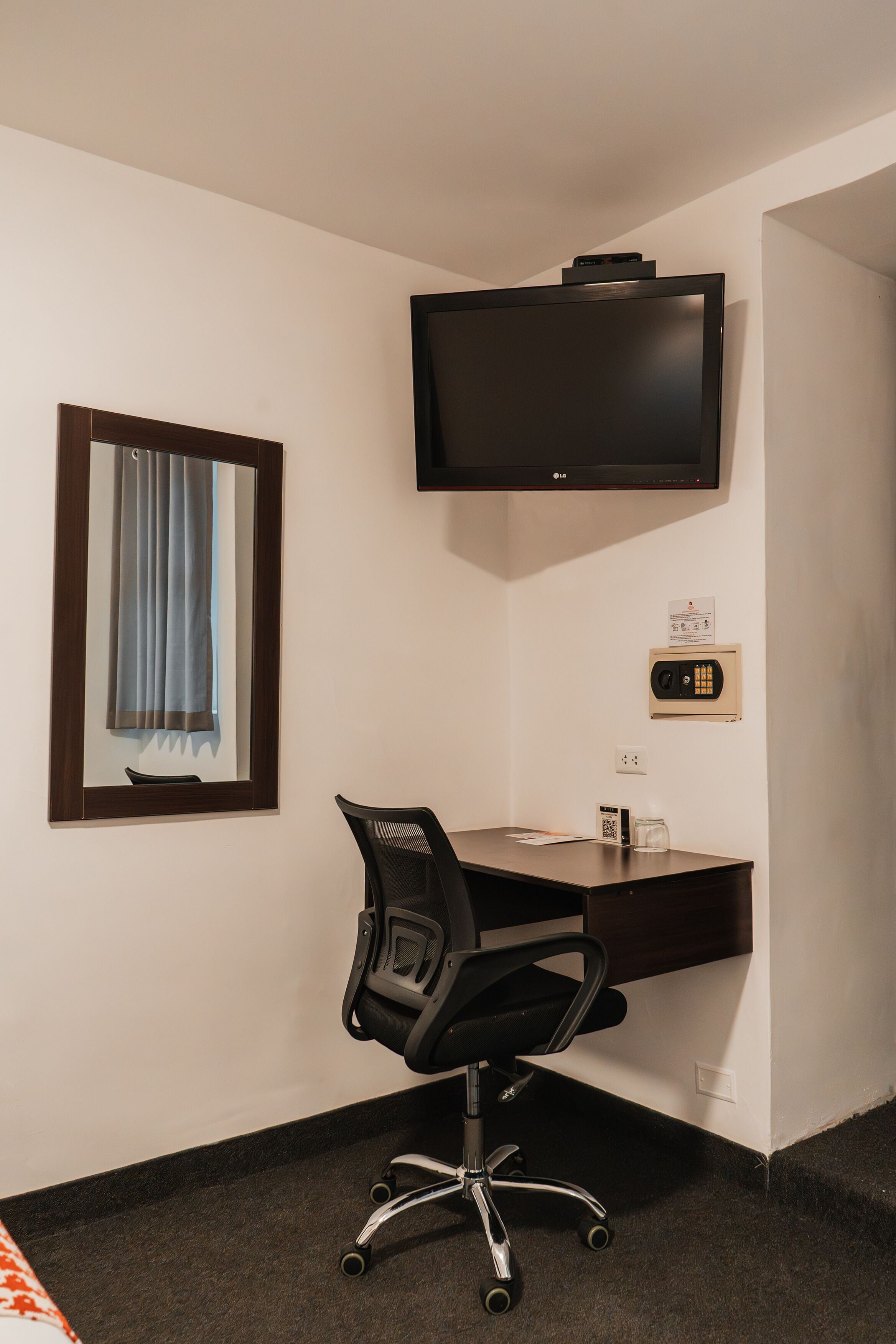 A hotel room with a desk, chair, television, and a window with curtains.
