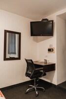 A hotel room with a desk, chair, television, and a window with curtains.