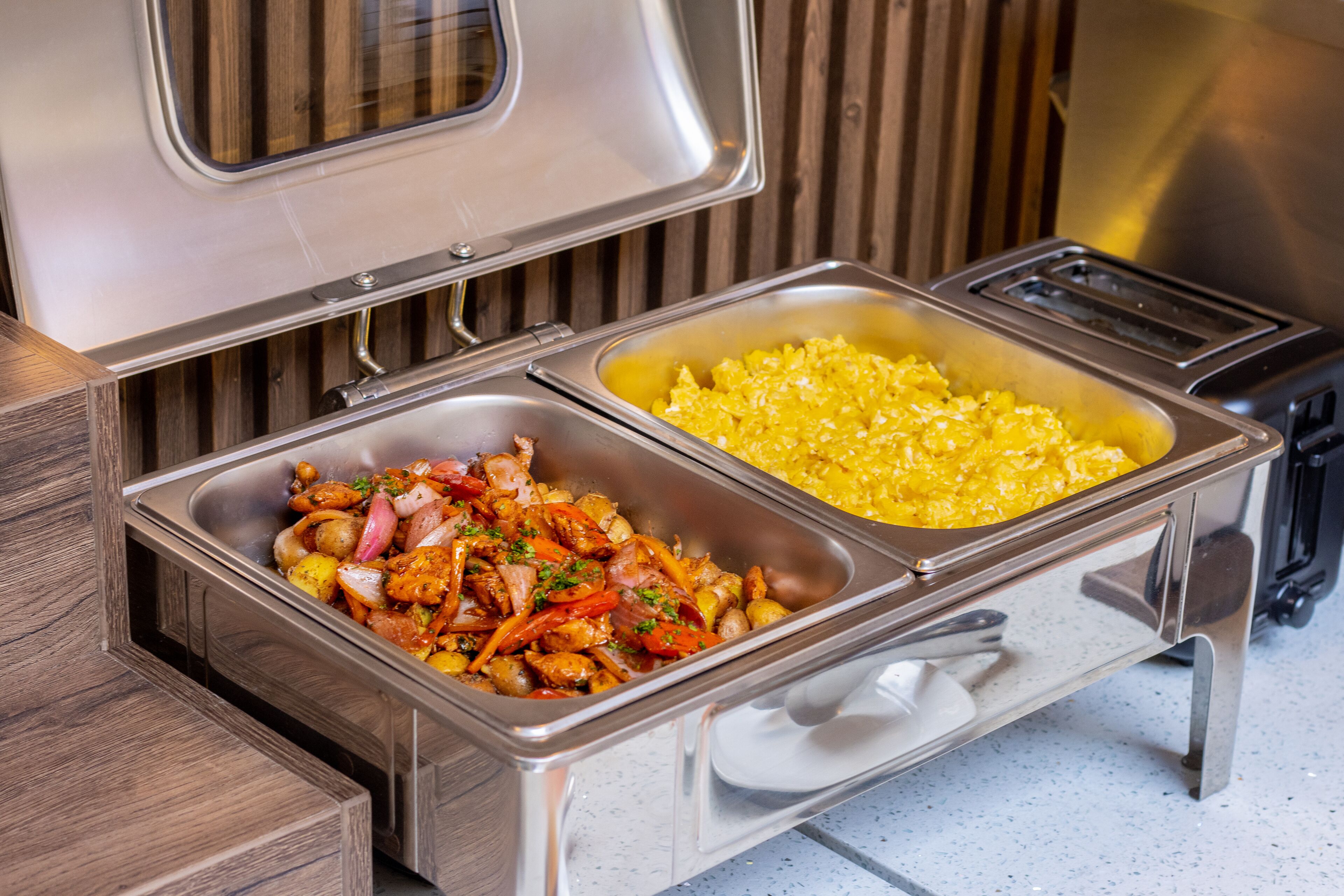 A buffet with two metal serving trays, one with a yellow dish and the other with a mixed dish.