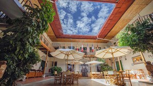 Un patio interior con mesas y sillas de madera, sombrillas y plantas en macetas.