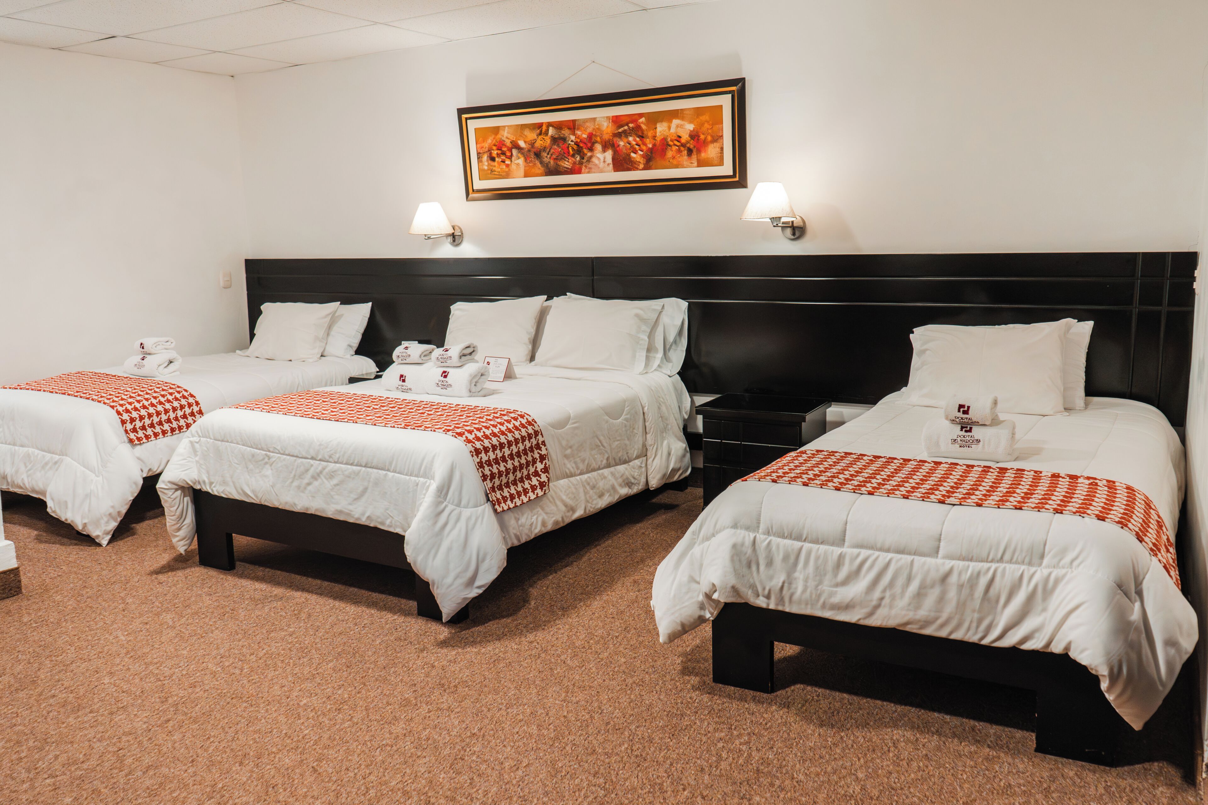 Ein Hotelzimmer mit drei Betten, jedes mit weißer Bettwäsche und orangefarbenen Akzenten, einem dunklen Kopfteil und einem Bild darüber.