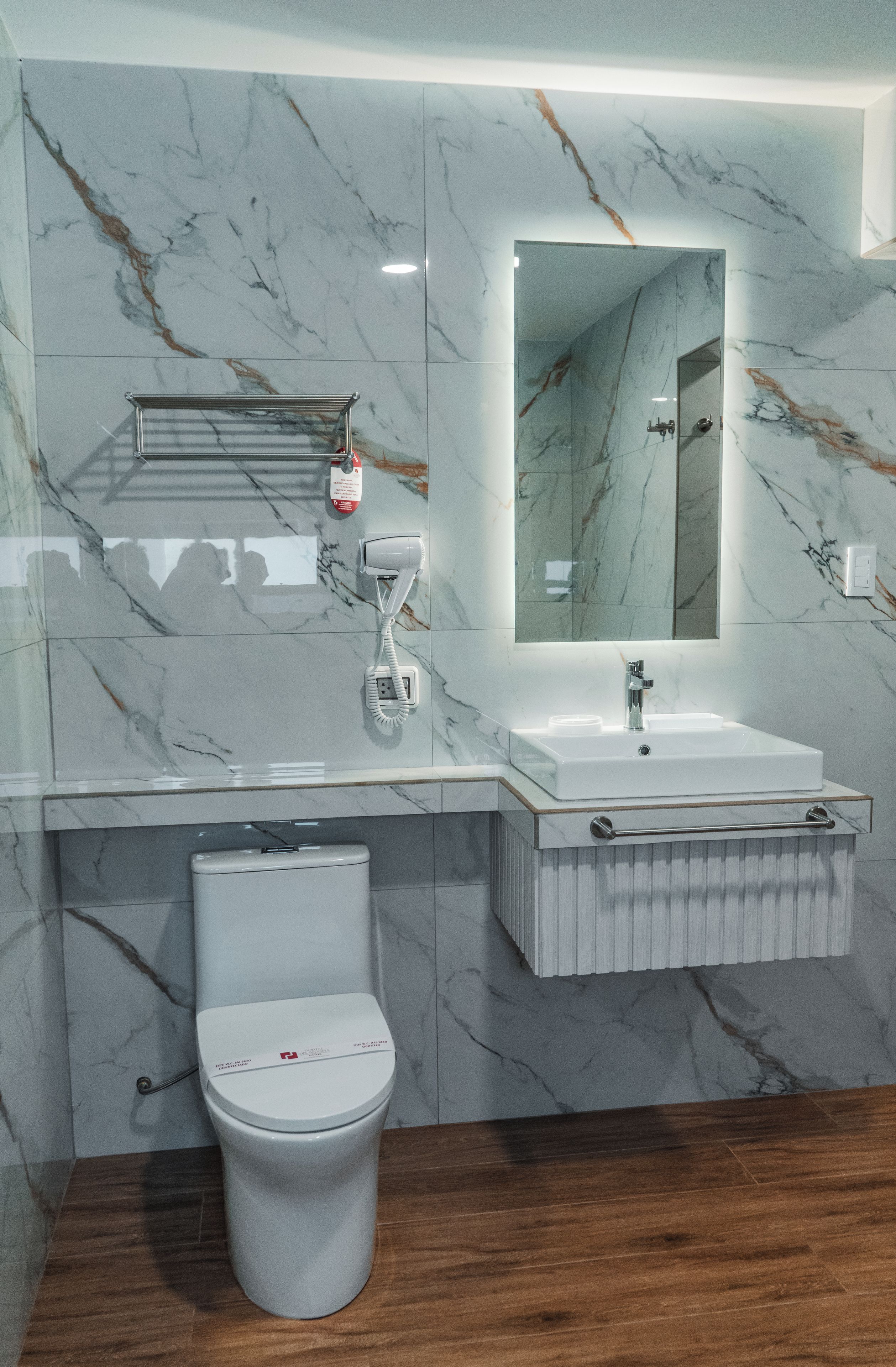 A bathroom with a marble wall, a white sink, a mirror, and a toilet.