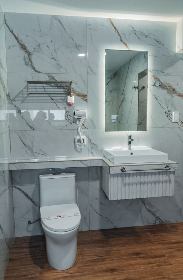 A bathroom with a marble wall, a white sink, a mirror, and a toilet. - Hotel El Portal Del Marques (Cajamarca)