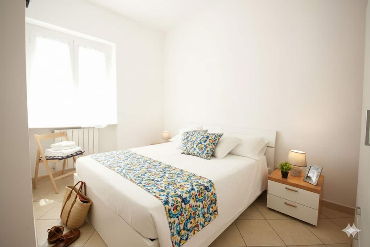 Una camera da letto ordinata con un letto, un comodino, una lampada e una sedia con asciugamani piegati.