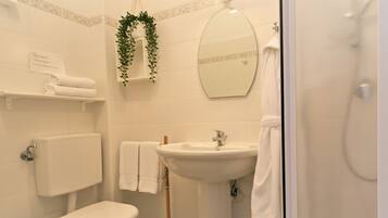 Une salle de bain avec des toilettes, un lavabo et une douche. Il y a des serviettes et un miroir au mur.