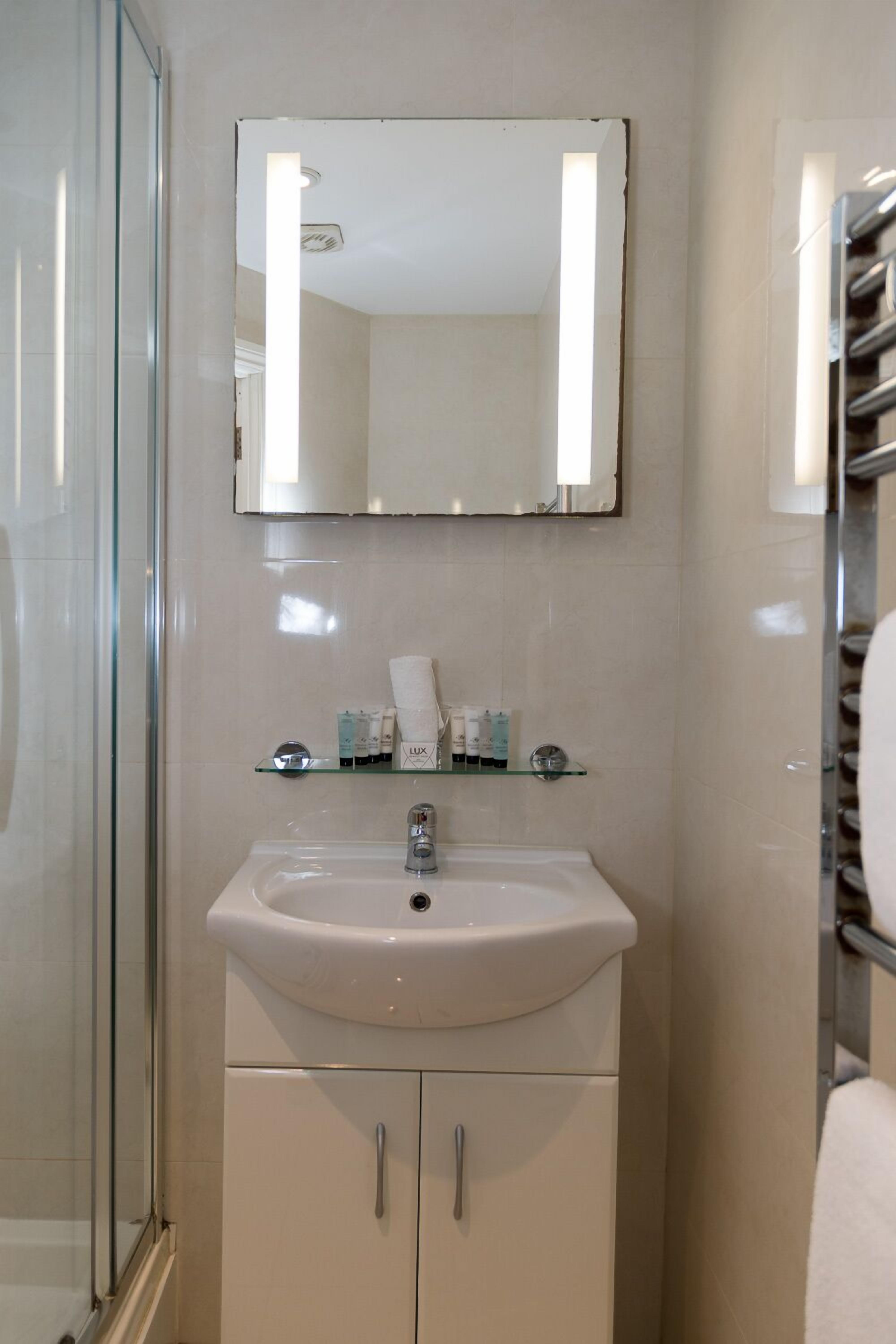 A bathroom with a glass shower enclosure, a white sink with a mirror above it, and a towel rack to the right.
