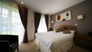 Habitación de hotel con una cama grande, una mesita de noche de madera, una lámpara y un cuadro en la pared.