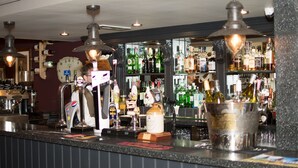 Zona de bar con múltiples grifos, un reloj y estantes llenos de diferentes botellas.