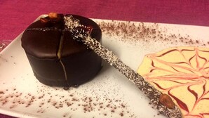 A chocolate-covered dessert on a plate with a decorative design. - Logis Hôtel les Terrasses (Longpont)