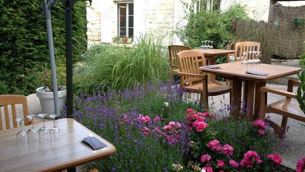 An outdoor seating area with wooden tables and chairs, surrounded by a variety of flowers and plants. - Logis Hôtel les Terrasses (Longpont)