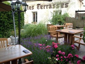 Un espacio al aire libre con mesas y sillas de madera, rodeado de diversas flores y plantas.