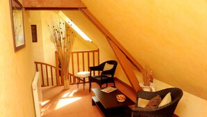 A cozy attic room with a wooden staircase, a dining table with chairs, and a wicker chair with cushions. - Logis Hôtel les Terrasses (Longpont)