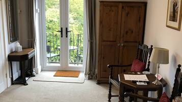 A room with a wooden wardrobe, a desk with a lamp, a chair, a small table, and a balcony door.
