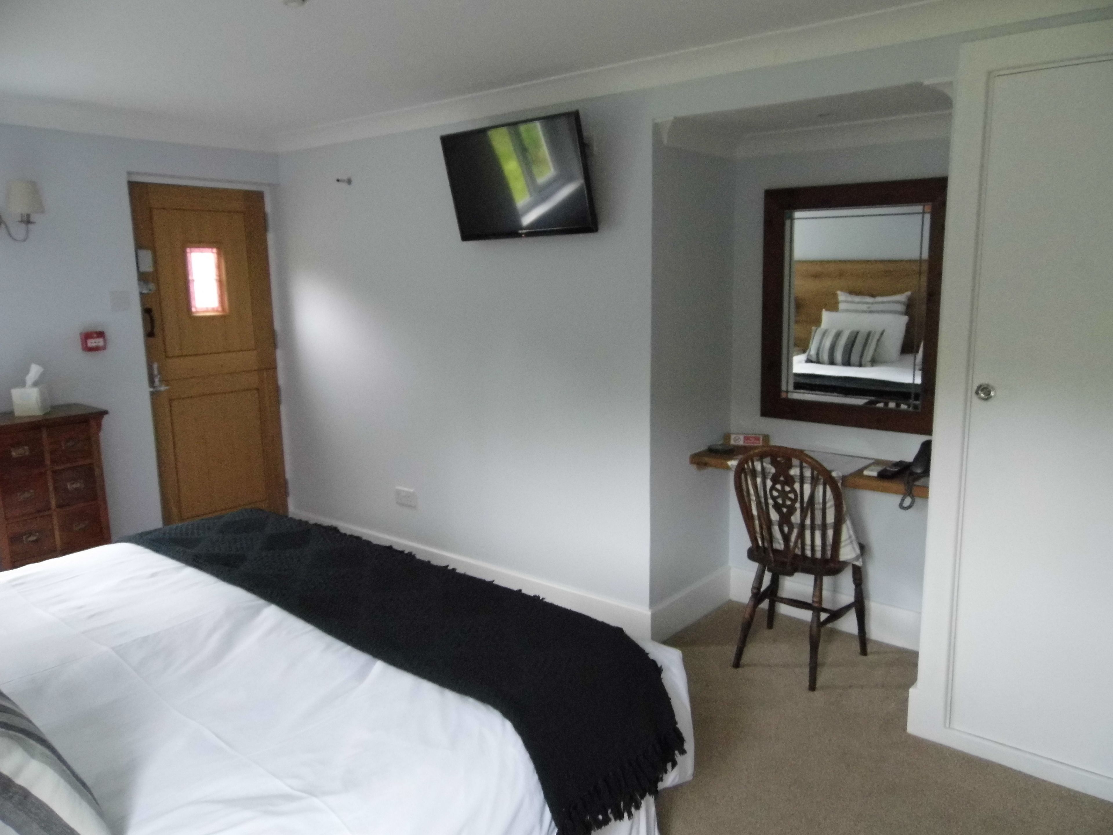 A bedroom with a bed, a desk, a chair, a television, and a door.