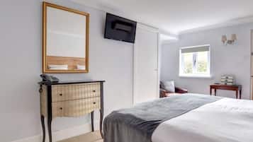 Un dormitorio con cama, mesita de noche con lámpara, cómoda, televisor montado en la pared y ventana que proporciona luz natural.