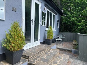 A house with a stone staircase leading to a door, two potted plants, and a small outdoor seating area. - The Mill at Glynhir (Ammanford)