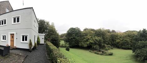 A two-story white building with a stone wall and a gravel pathway leading to a green lawn.
