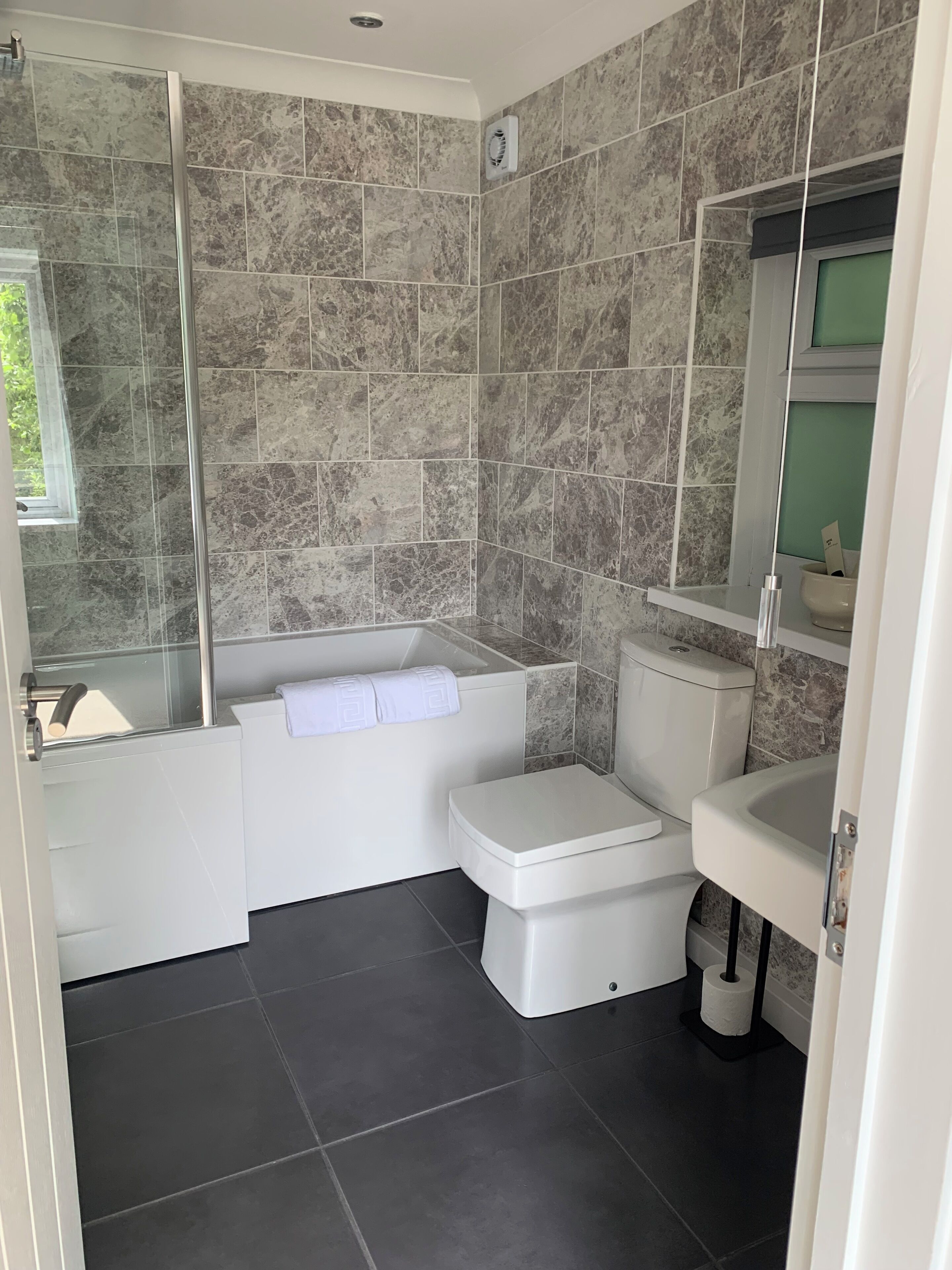Ein modernes Badezimmer mit Duschkabine aus Glas, einer weißen Badewanne, Toilette und Waschbecken.