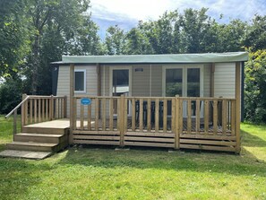 A small, single-story mobile home with a wooden deck and a covered porch.