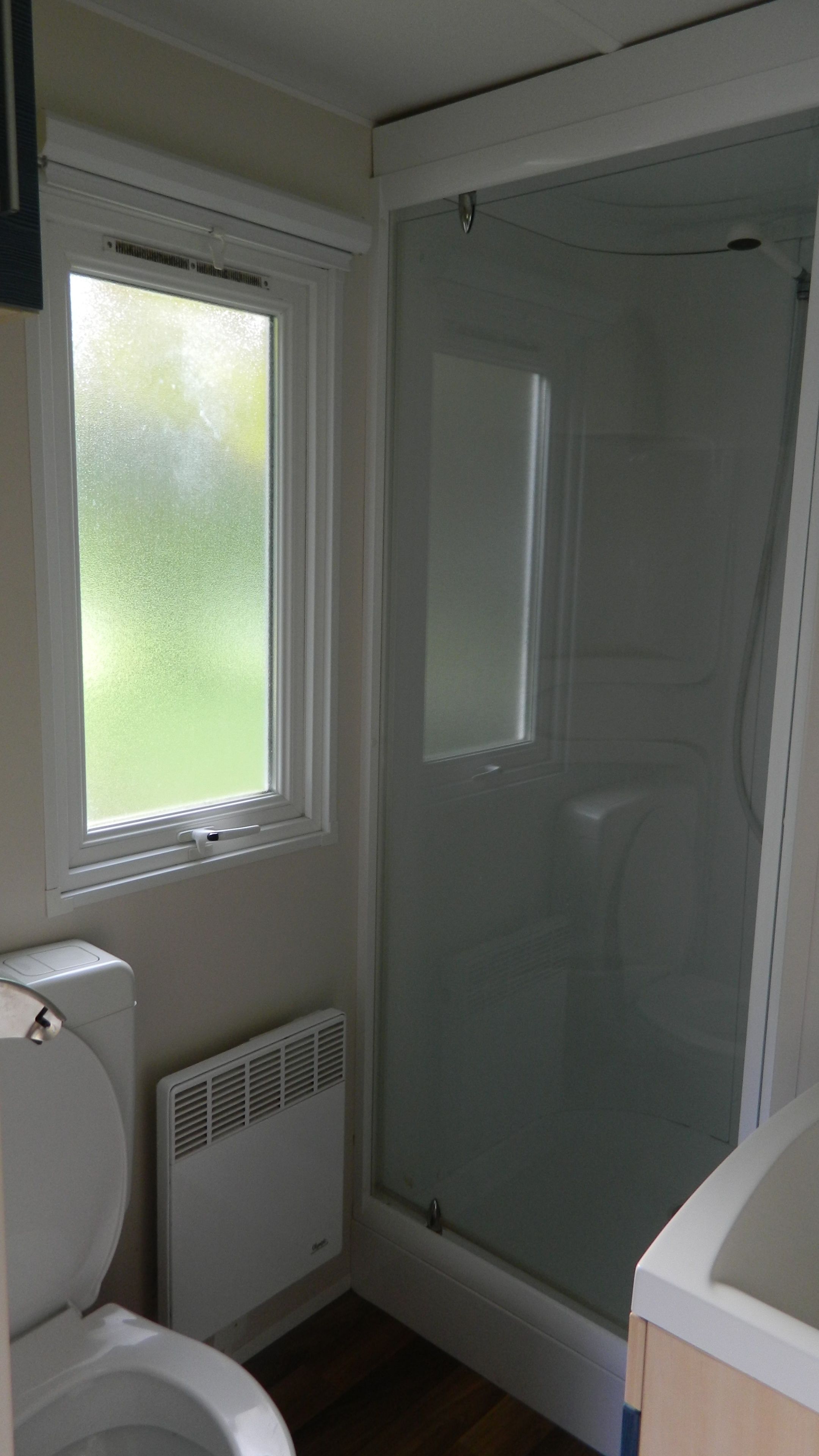 Un baño con inodoro, ventana, cabina de ducha y radiador.