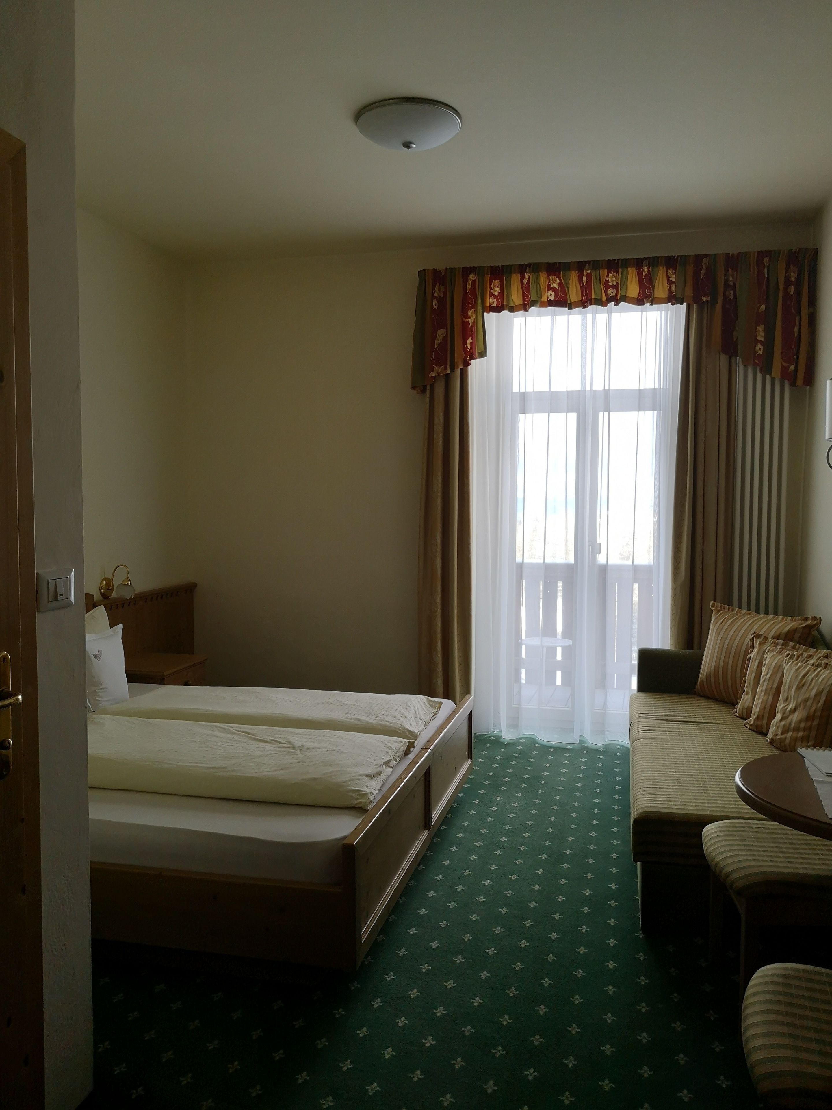 A hotel room with a bed, a sofa, a small table, and a window with curtains.