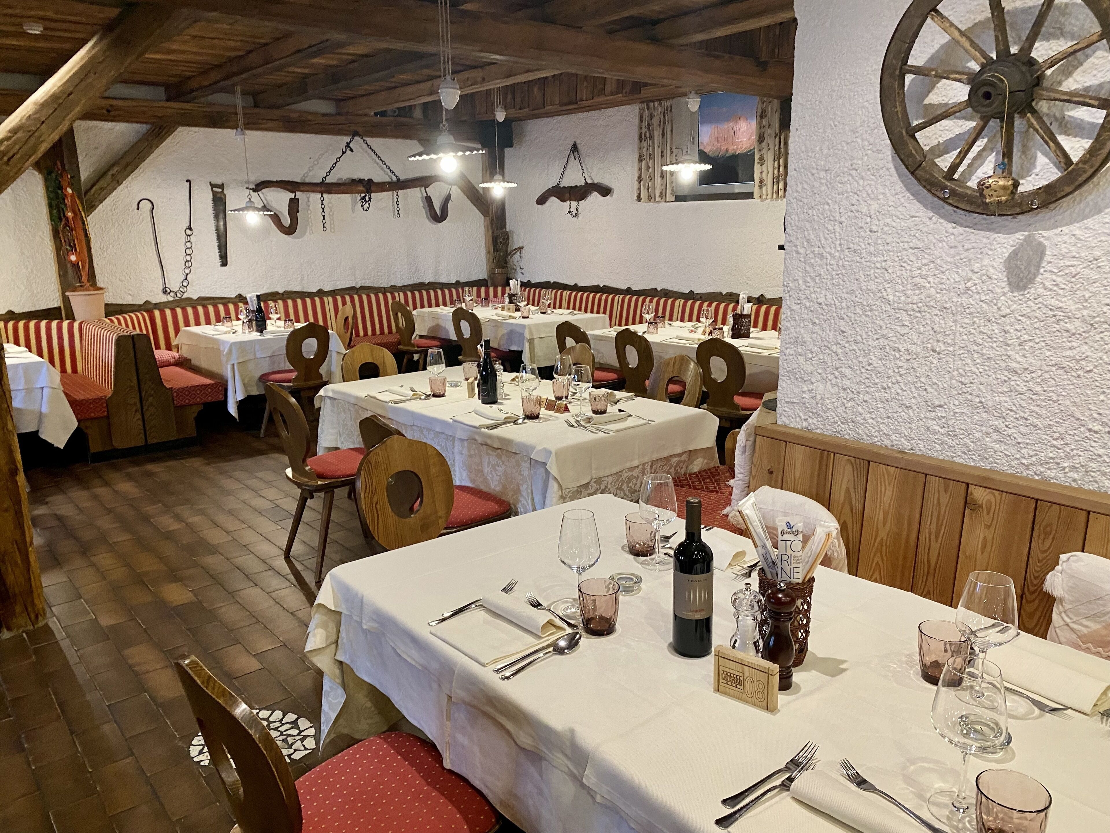 A restaurant with wooden benches and tables, some with wine glasses and bottles.