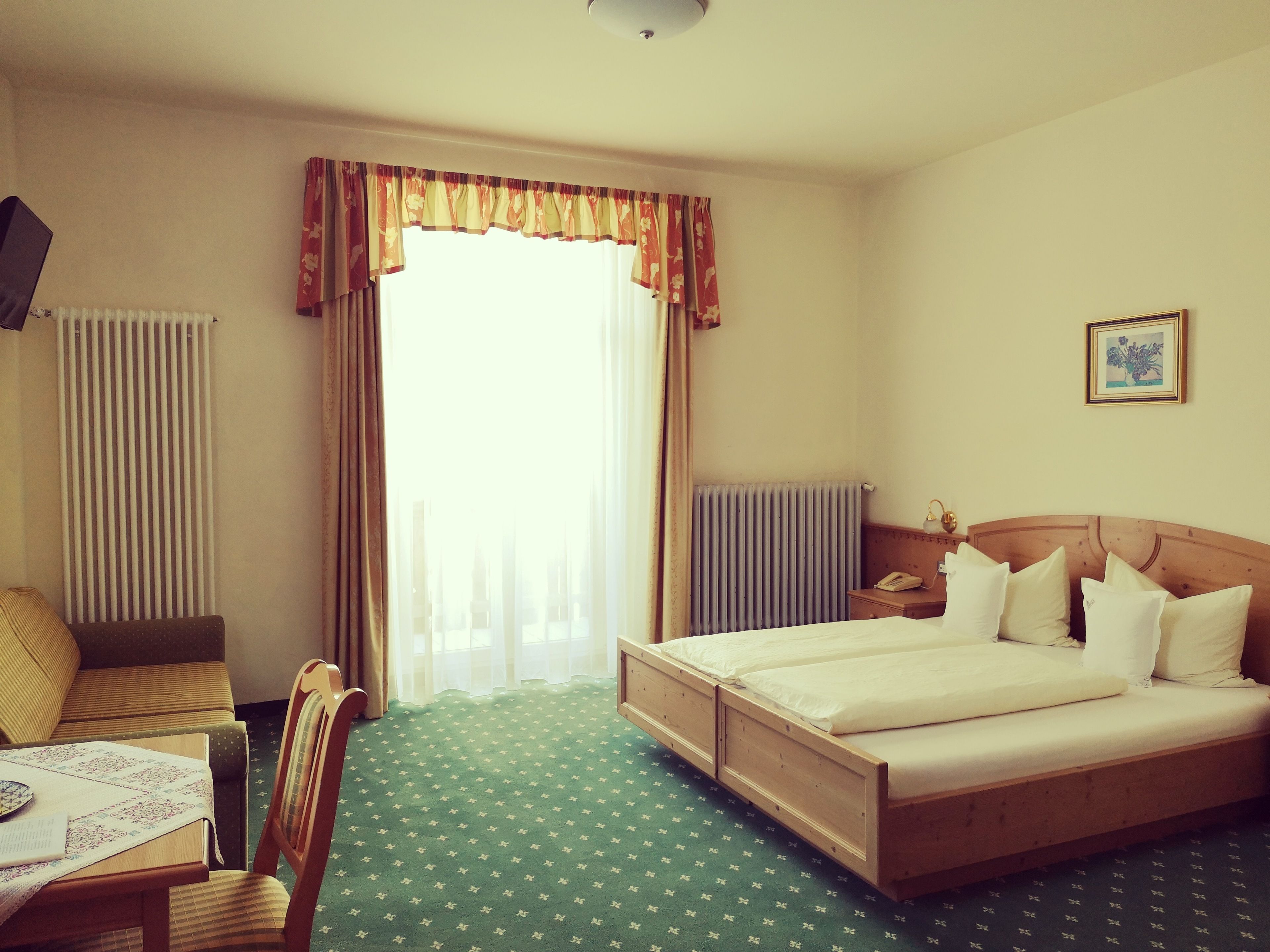 A hotel room with a bed, a chair, a table, and a window with curtains.