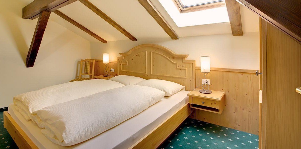 A bedroom with a wooden bed, two bedside tables with lamps, a skylight, and a wooden wardrobe.
