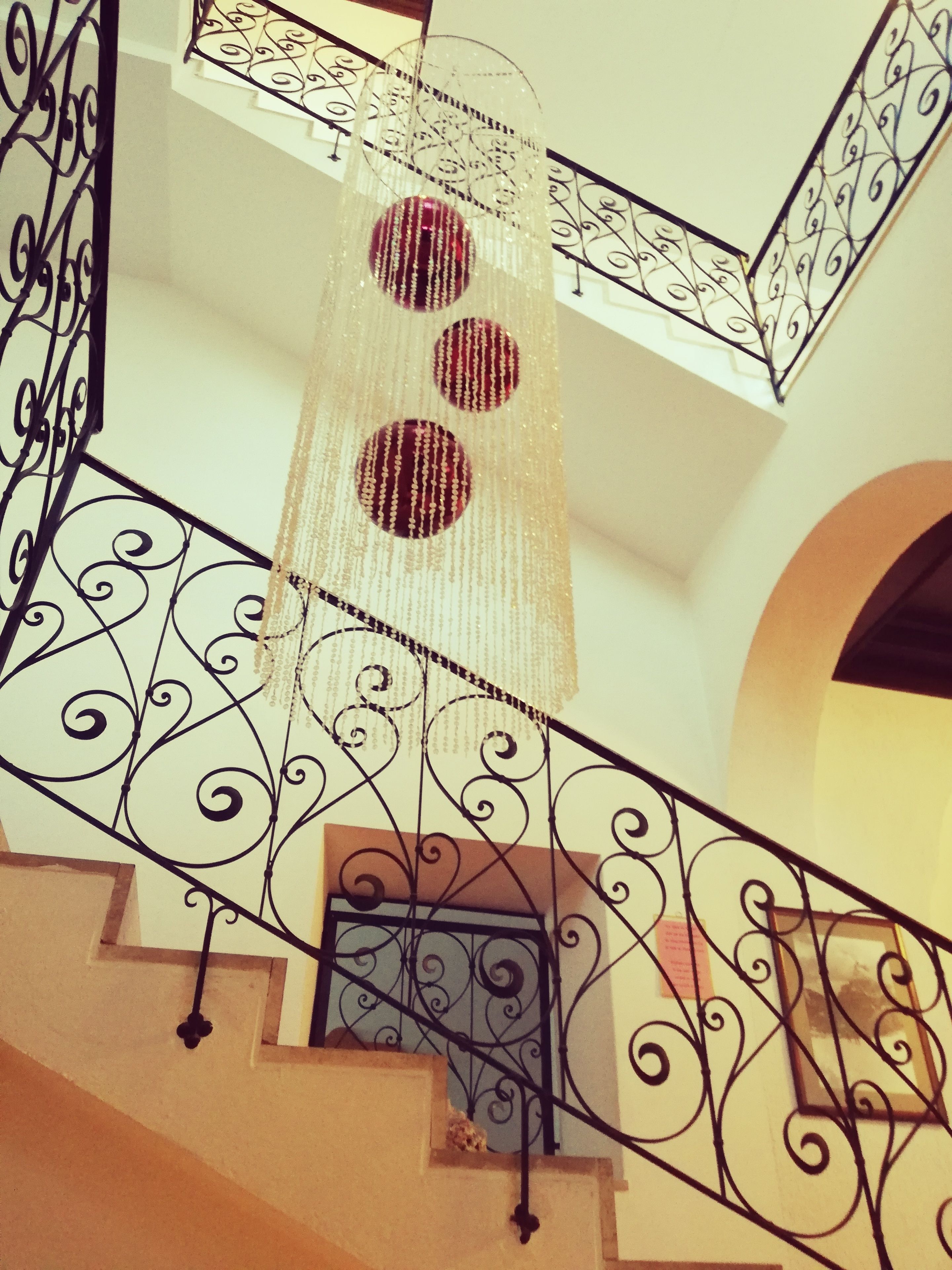 A staircase with ornate black metal railings and a decorative hanging light fixture with three spherical ornaments.