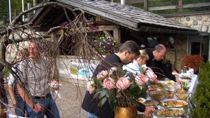 Una mesa de buffet con diferentes platos de comida, un jarrón grande con flores rosadas y un rústico edificio de piedra al fondo.