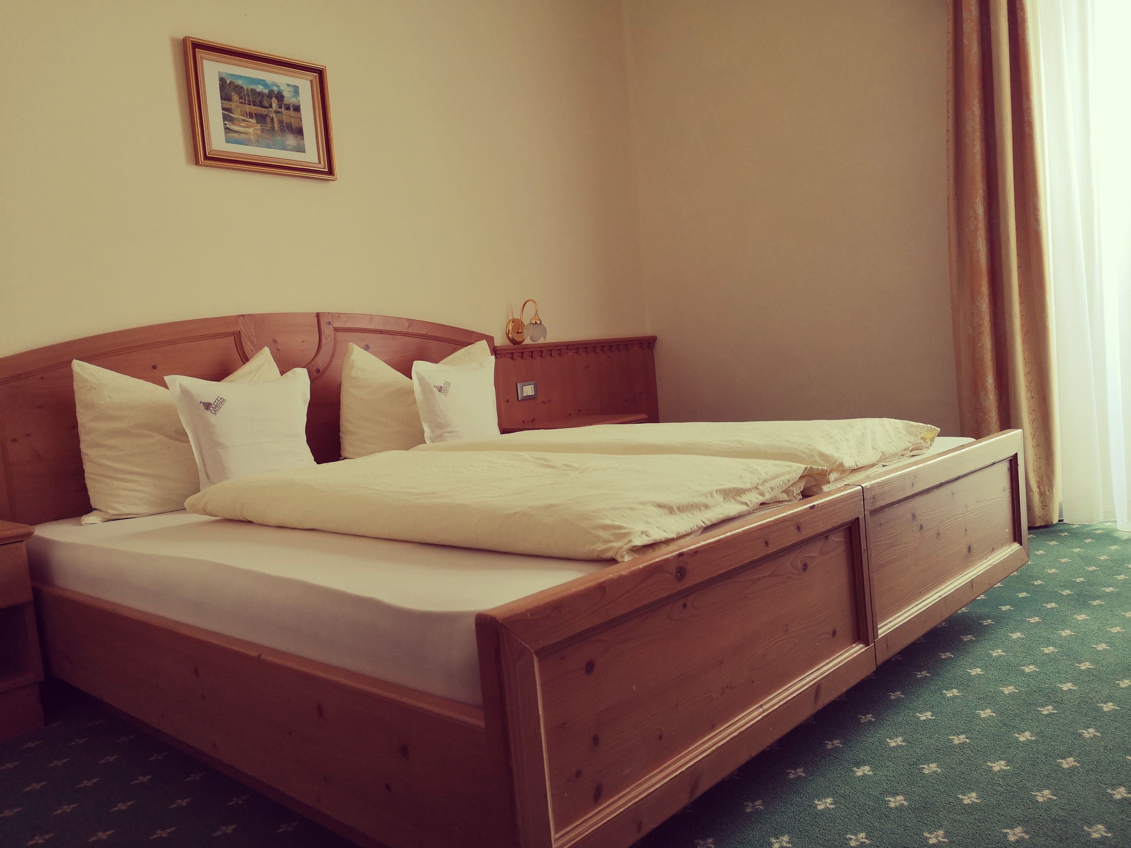 A wooden bed with white bedding in a room with a green carpet.