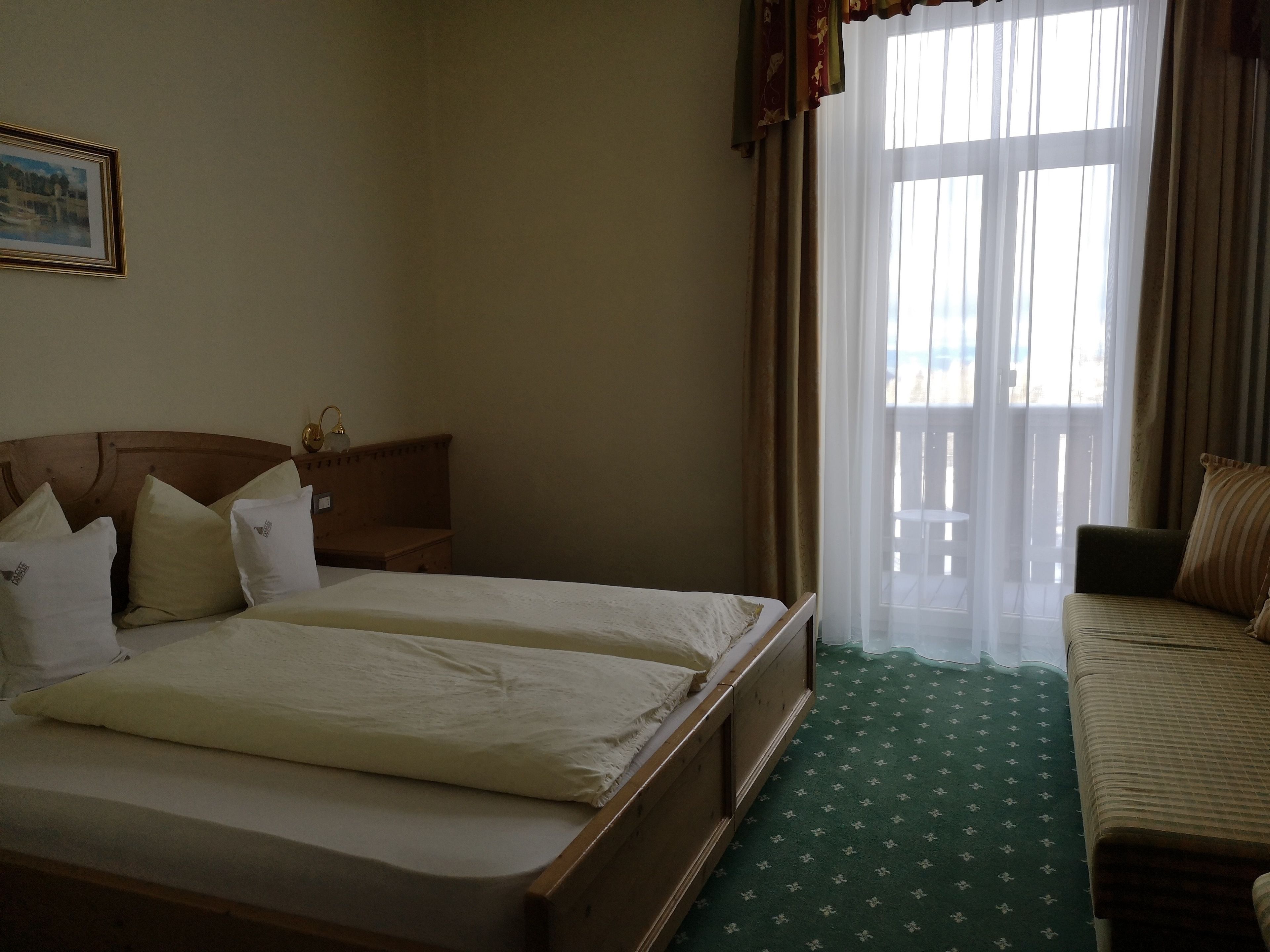 A hotel room with a large bed, a smaller bed, a sofa, a nightstand, a lamp, and a window with curtains.